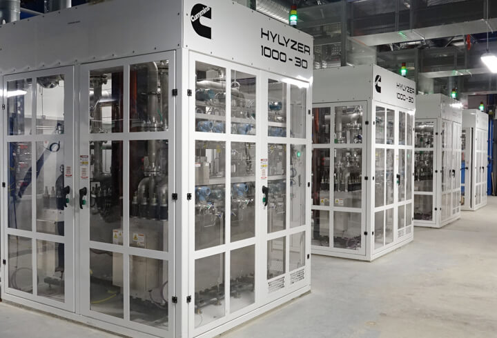 Four eletrolyzers side-by-side, which look like glass boxes the size of a garden shed.
