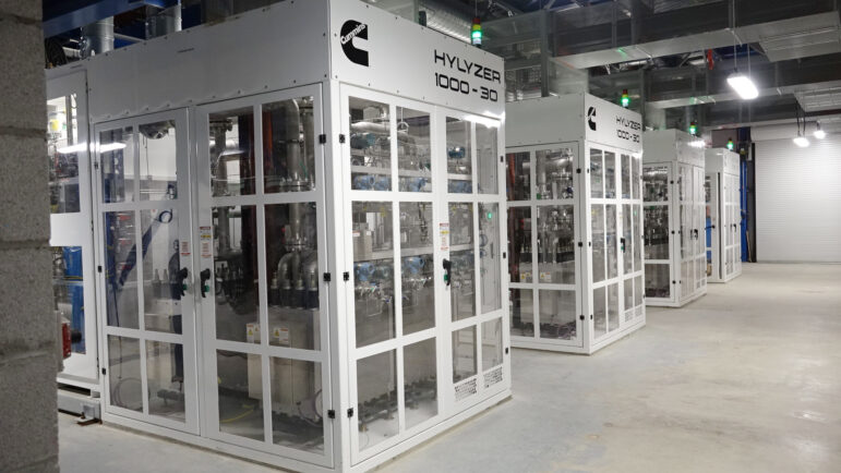 Four eletrolyzers side-by-side, which look like glass boxes the size of a garden shed.