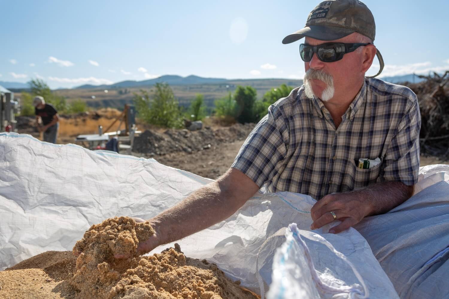 A person picks up a handful of sawmill dust and examines it.